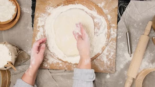 Hands Dusting Dough with Flour on Wooden Board