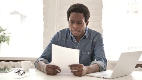 Young Man Reading Papers at Office Desk