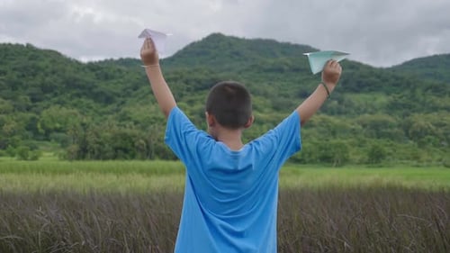 Boy Holding Paper Airplanes in Rural Field