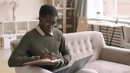 Young Adult Writing in Notebook with Laptop