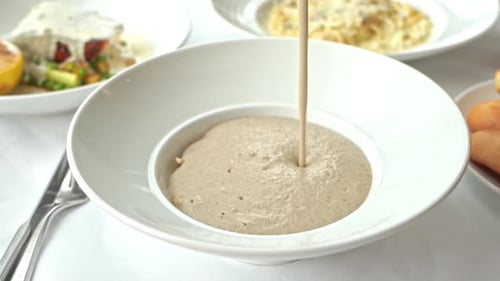 Pouring Savory Soup Into a Bowl on Table