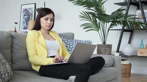 Shocked Woman Using Laptop on Couch at Home