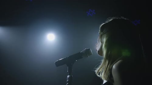 Close-up of the Face of the Singer with Microphone on a Black Smoky Background. The Singer Sings a