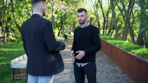 Porträt eines gutaussehenden bärtigen jungen Mannes im Gespräch mit einem Freund, der im Sommer-Frühling im Stadtpark steht