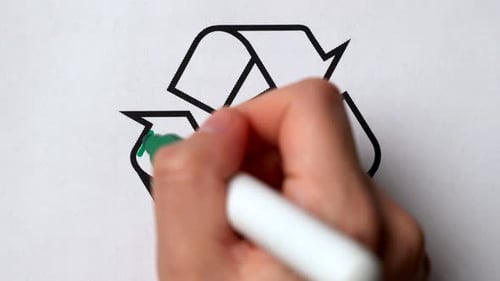 La mano con un marcador verde rodea un letrero de reciclaje de basura en papel blanco