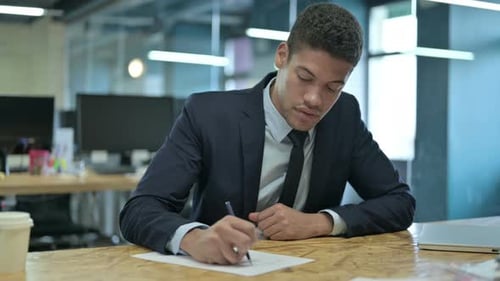 Young African Businessman Writing on Paper on Office Desk