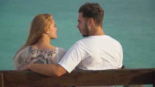 Man and Woman Talk Sitting at the Bench, Sea Is in the Background