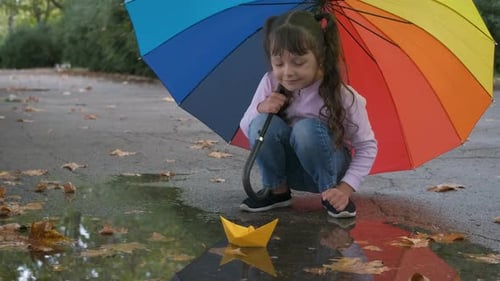Girl Plays with Paper Boat in Rainy Puddle