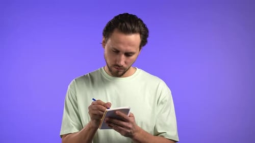 Man Writing in Notebook Against Purple Backdrop