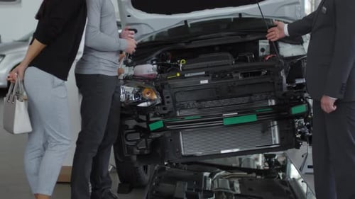 Seller Telling about Car Engine to Couple in Auto Dealership Showroom