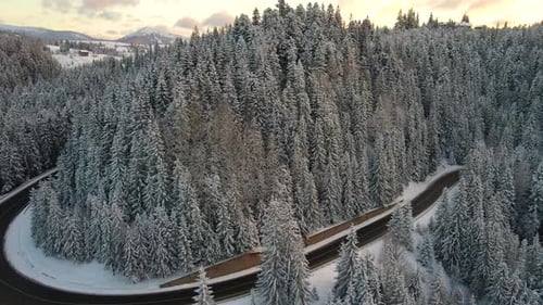 Aerial view of winter landscape with snow covered mountain hills and winding forest road in morning.