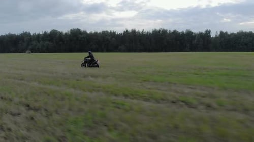 Motorcyclist Rides Across Grassy Field in Rural Landscape
