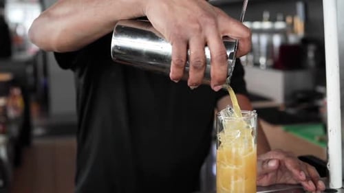 Orangencocktail wird in Zeitlupe über Eiswürfel in ein hohes Glas gegossen