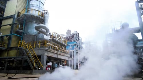 Dense white steam on territory of an oil refinery. Stairs at large oil pipeline