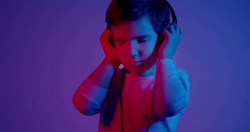 Boy Listens to Music on Headphones with Neon Lighting