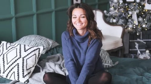 Smiling Woman Sits on Bed Near Christmas Tree