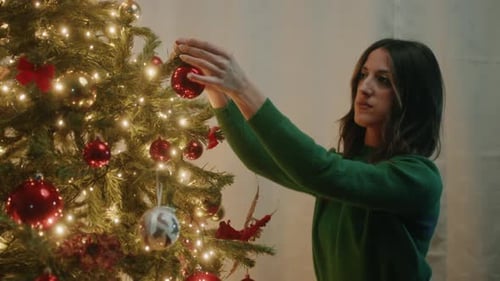Woman Decorating Christmas Tree with Ornaments at Home