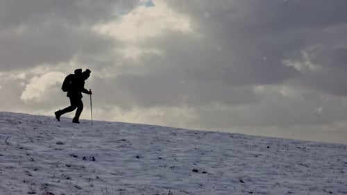 Silhouette Hiker Ascending Snowy Hill in Winter