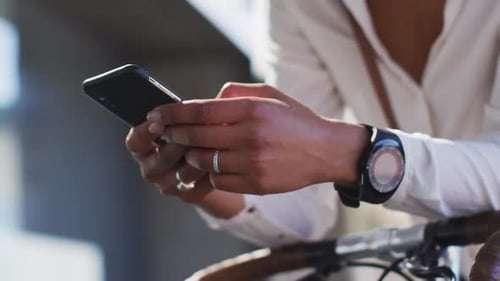 Midsection of african american woman using smartphone leaning on bike in street