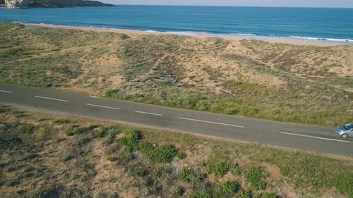 Car Driving Slow at Beach Road Near Turquoise Calm Sea Waters and Golden Sand Dunes in Alepu Beach