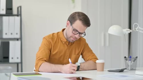 Young Man Writing on Paper in Office