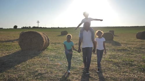 Darkskinned Family Walking Across Field at Sunset