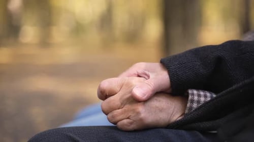Joined Hands of Aged Couple Sitting in Autumn Park