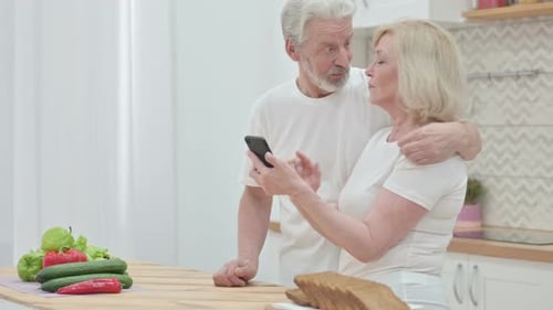 Senior Couple Laughing at Mobile Phone in Kitchen