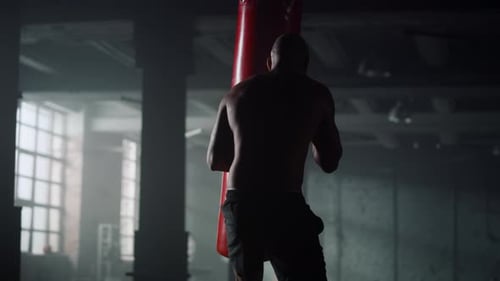 Muscular Man Punches Punching Bag in Gym