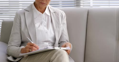 Woman Writing on Clipboard Sits on Couch