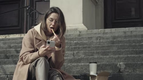 Woman Using Smartphone on City Steps with Food