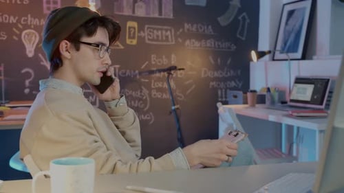 Male Employee Speaking on Mobile Phone and Checking Papers Working in Dark Office