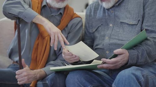 Two Unrecognizable Caucasian Men Watching Old Photos. Male Grey-haired Retirees Recalling Memories