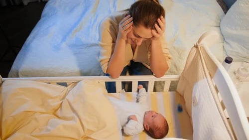 Tired Woman Watches Baby in Crib