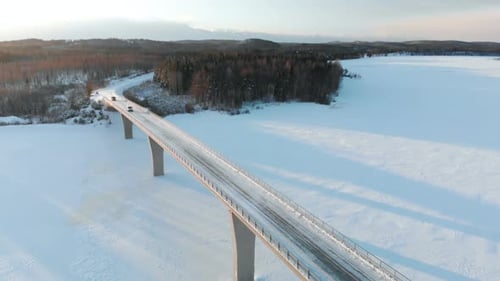 Bridge over frozen water and some cars passing seen from a drone