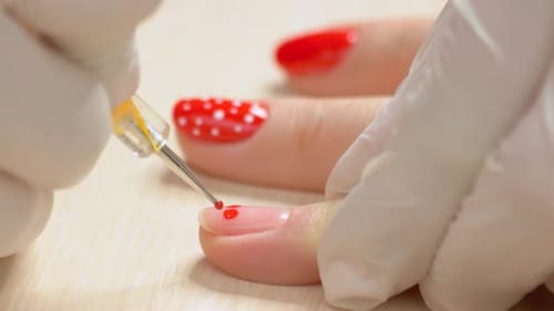 Manicurist applies red nail polish to fingernail