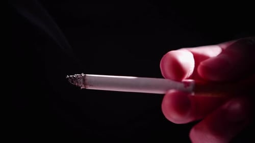 Hand Holding Lit Cigarette on Black Background