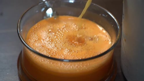 Jus de carotte et d'orange frais versé dans un bol en verre de la machine à jus - Ralenti