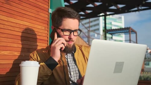 Man Working On Laptop And Talking On Phone Outdoors