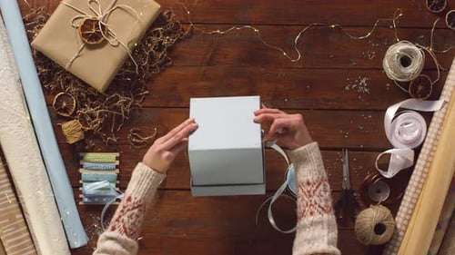 Woman Wrapping Holiday Gift with White Ribbon Overhead