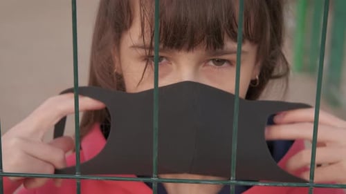 Child Puts on Mask Behind Metal Fence