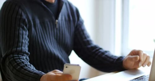 Man Uses Laptop and Smartphone at Table