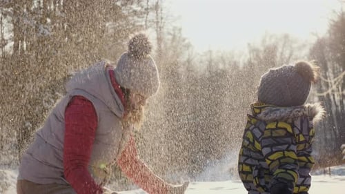 Glückliche Mutter mit kleinem Sohn spielt mit Schnee und wirft es hoch