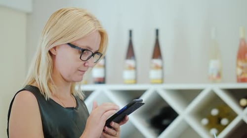 Portrait of a Young Woman in Glasses, Uses a Smartphone While Waiting for Her Order in a Cafe
