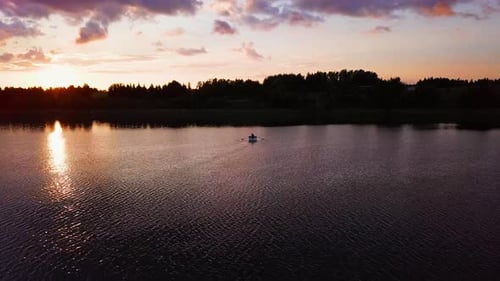Peaceful sunset on a lake. Man on a paddle boat. Beautiful colours. Relaxing scenery. Drone shot.