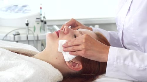 Woman Cleaning Face with Cotton Pad in Clinic
