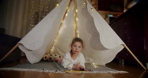 Girl Plays on Tablet in Cozy Illuminated Tent