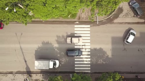Vista aérea de cima para baixo da rua com carros em movimento e faixa de pedestres com pedestres cruzando.
