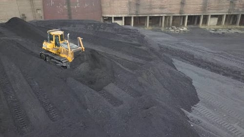 Bulldozer-Traktor sammelt schwarze Kohle auf dem Versorgungsfeld eines thermoelektrischen Kraftwerks