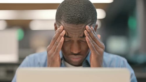 Tired Young Adult Rubbing Forehead at Desk